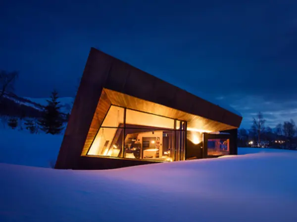 moderne hytte omgitt av snø om vinteren med full belyning inne