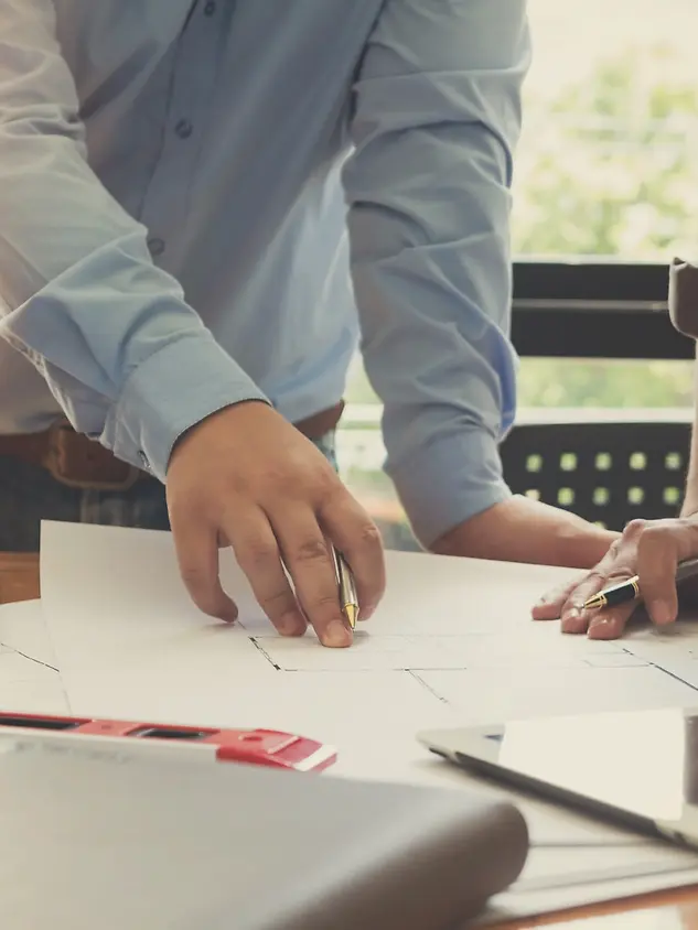 Due progettisti analizzano elaborati tecnici e schemi costruttivi su un tavolo, durante una fase di progettazione