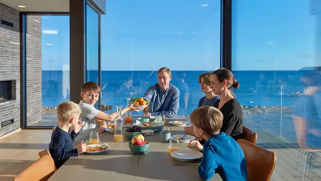 Famiglia riunita a tavola in un ambiente luminoso con vista mare, simbolo della qualità e del comfort delle soluzioni Schüco.