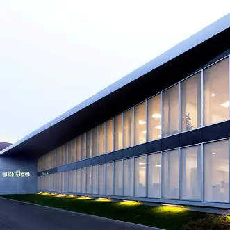 Vista prospettica della sede Schüco Italia con facciata continua vetrata e illuminazione serale