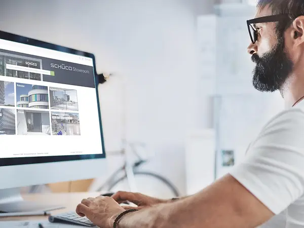 Architetto al computer mentre consulta il Catalogo BIM Schüco per la progettazione di facciate, finestre e porte
