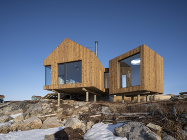 Modernes Holzhaus auf Stelzen mit großen, bodentiefen Schüco Fenstern in felsiger Landschaft