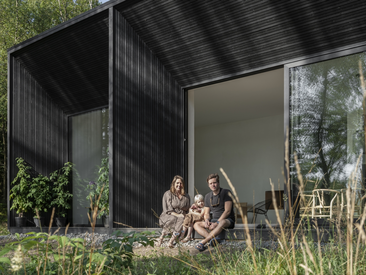 Familie vor einer geöffneten, raumhohen Schüco Schiebetür an einem modernen Wohnhaus in naturnaher Umgebung