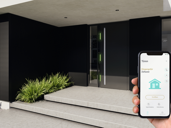 Smartphone zur Steuerung von Schüco Türen und Fenstern vor modernem Hauseingang