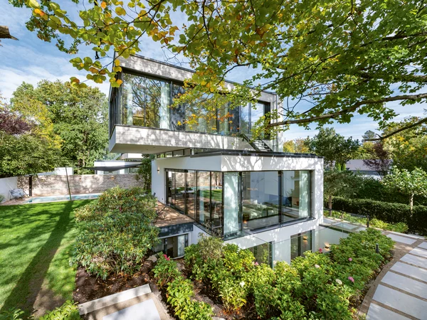 Modernes Wohnhaus mit vielen großflächigen Schüco Fenstern, umgeben von einem grünen Garten