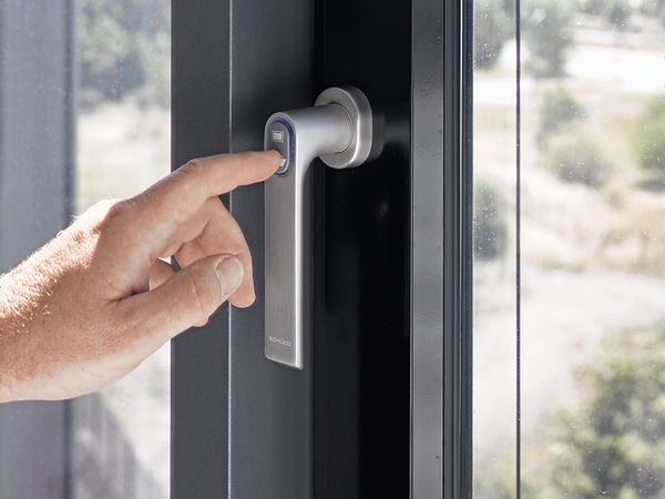 Hand bedient einen automatisierten Fenstergriff an einem Schüco Fenster zur smarten Fenstersteuerung