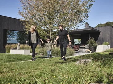 Familie im Garten ihres Neubau Wohnhauses mit Schüco Elementen